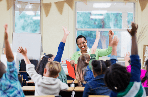Students raising their hands with a smiling teacher